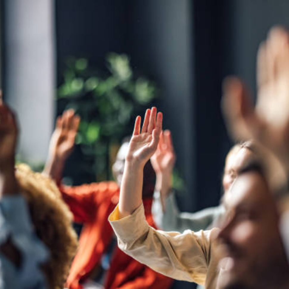 Group of people sitting on a seminar. They have their hand raised.